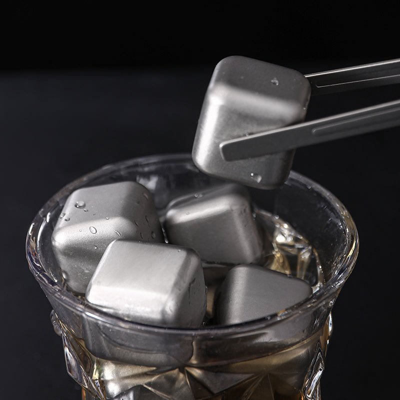Wiederverwendbare Titan-Würfel im Whiskeyglas, einer wird mit der Servierzange entnommen