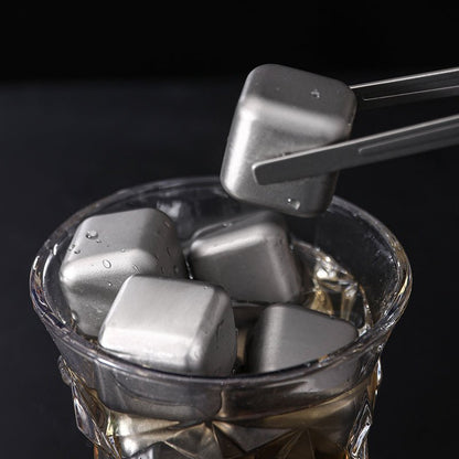 Wiederverwendbare Titan-Würfel im Whiskeyglas, einer wird mit der Servierzange entnommen